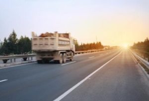 Preventing Commercial auto insurance claims | Photo of a commercial dump truck on the roadways driving towards a setting sun.