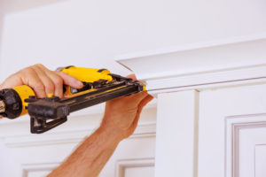 Artisan working with a brad nailer installing door trim on a construction site, representing artisan contractors insurance provided by Huff Insurance in Pasadena, MD