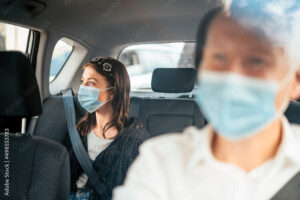 Two passengers in a car, both wearing protective face masks, demonstrating safety measures that relate to the Communicable Disease Auto Insurance Exclusion topic of the Huff Insurance blog.