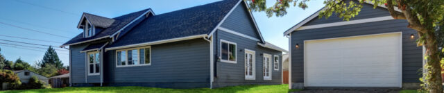 Gray house with a detached garage and a dirt driveway, surrounded by green grass and trees, illustrating a common residential property with separate structure, shich may be used for business purposes. | Huff Insurance Blog