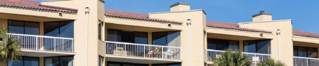 Exterior view of a beachfront condominium building with balconies and palm trees under a clear blue sky, representing Maryland condo living and insurance needs regarding the Maryland Condo deductible law
